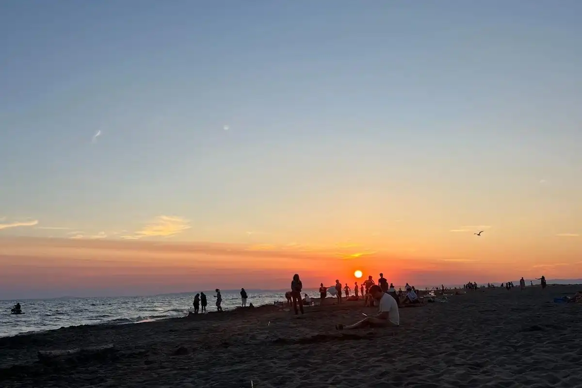 Coucher de soleil sur la mer avec des silhouettes de personnes sur la plage et le soleil orange près de l’horizon.