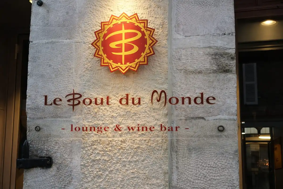 Enseigne lumineuse du Bout du Monde lounge & wine bar sur une façade en pierre de Beaune la nuit